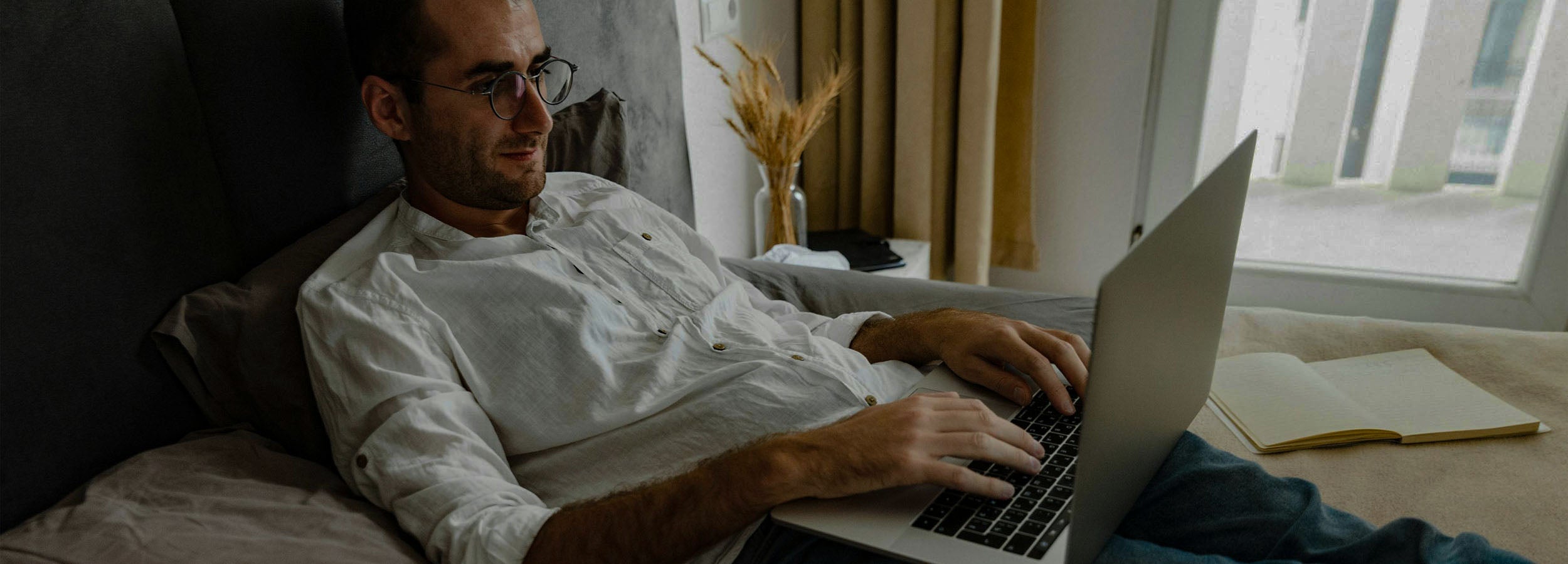 Middle-aged man working on a laptop while lying in bed, Neenca's guide to everyday movements that cause joint pain and how to fix them