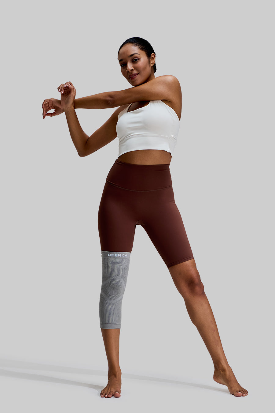 Full-body view of a female model stretching while wearing the grey NEENCA HX038 knee brace on her right leg
