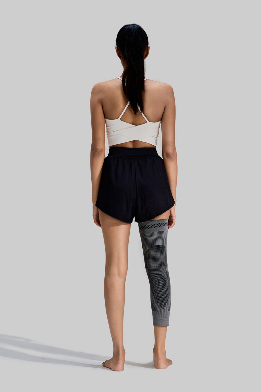 Full-length rear view of a female model wearing a grey NEENCA HX036 leg sleeve on her right leg