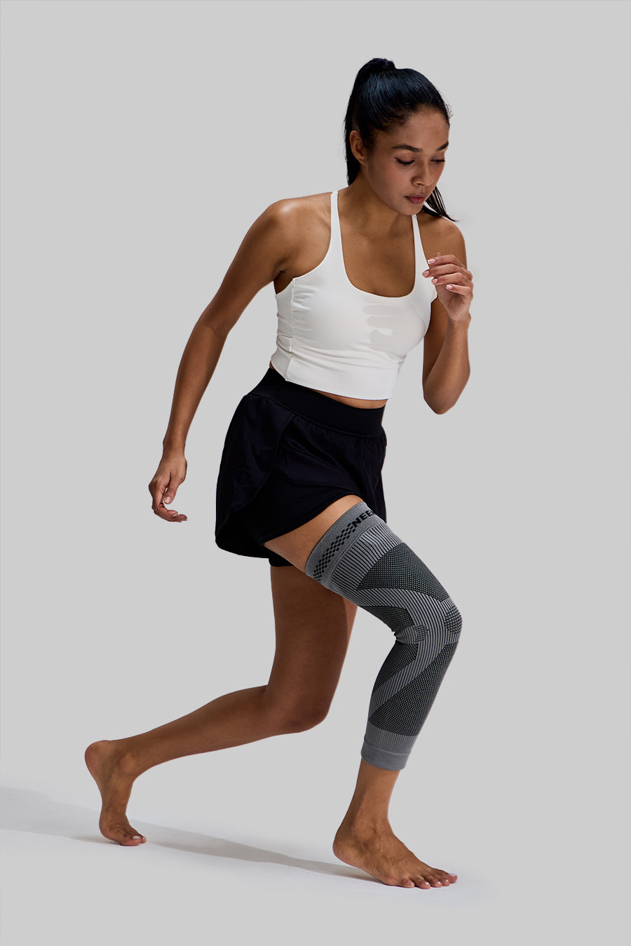 Female model in a running pose wearing a grey NEENCA HX036 leg sleeve on her right leg, showcasing the product's compression support during active movement