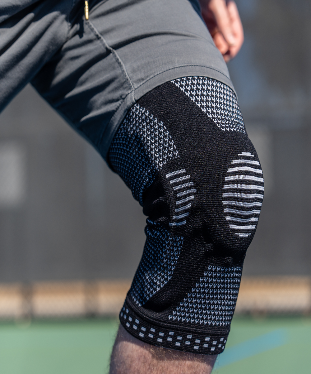 Close-up of a person wearing black knee pads with white patterns on a blurred background.