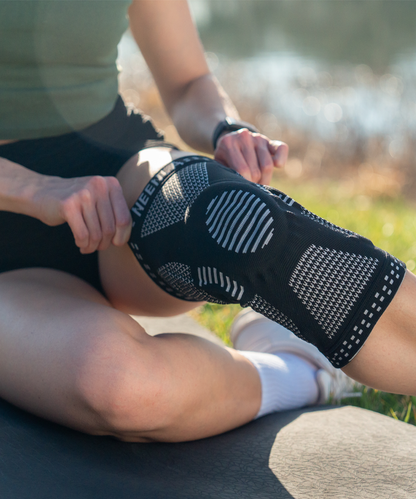 Person wearing a neenca black knee brace outdoors on a grassy area