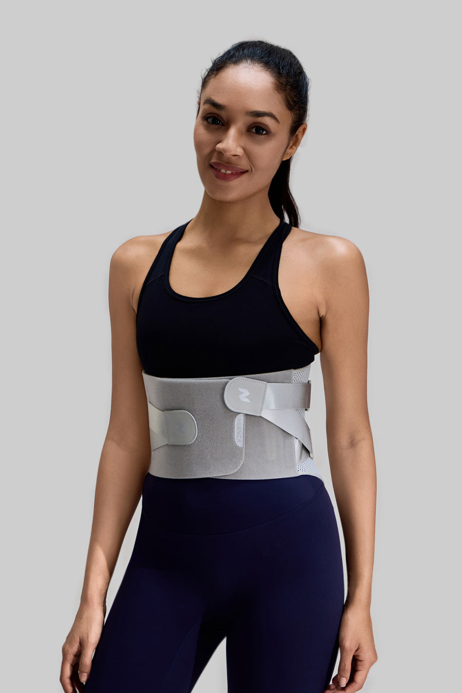 Smiling female model wearing NEENCA HY008 back brace over sports gear, showcasing the front fit and adjustable straps