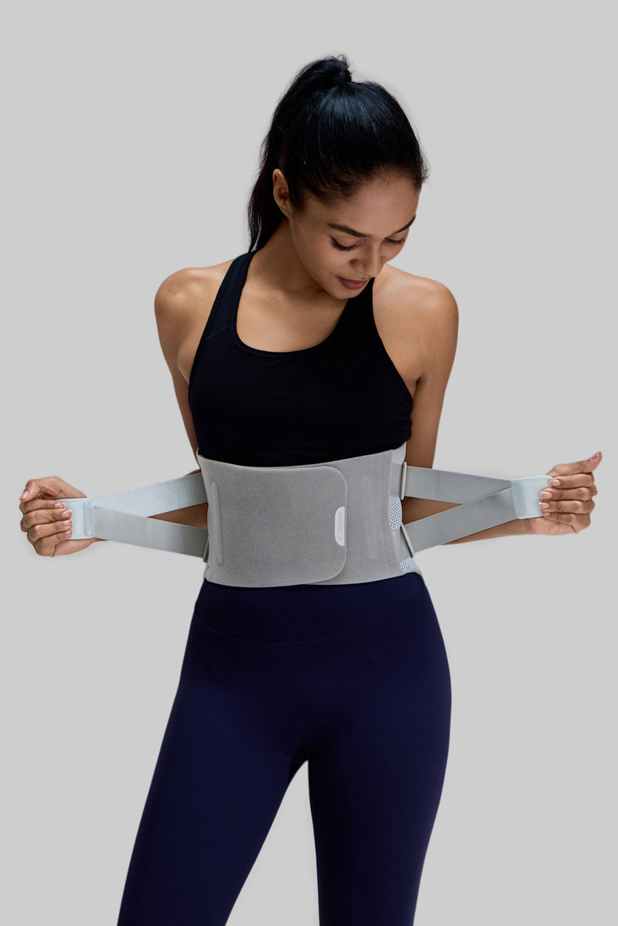 Female model demonstrating how to pull the adjustable elastic straps of the NEENCA HY008 back brace for customized compression
