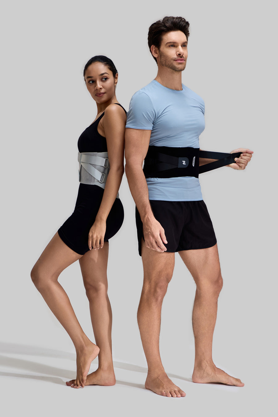 Male and female models standing back-to-back wearing NEENCA HY008 back braces in black and grey, showing the adjustable compression straps and universal fit