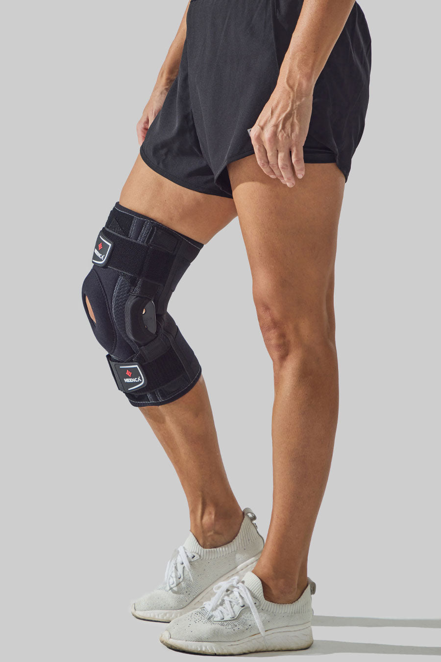 Model demonstrating knee flexion while wearing a black hinged knee brace.