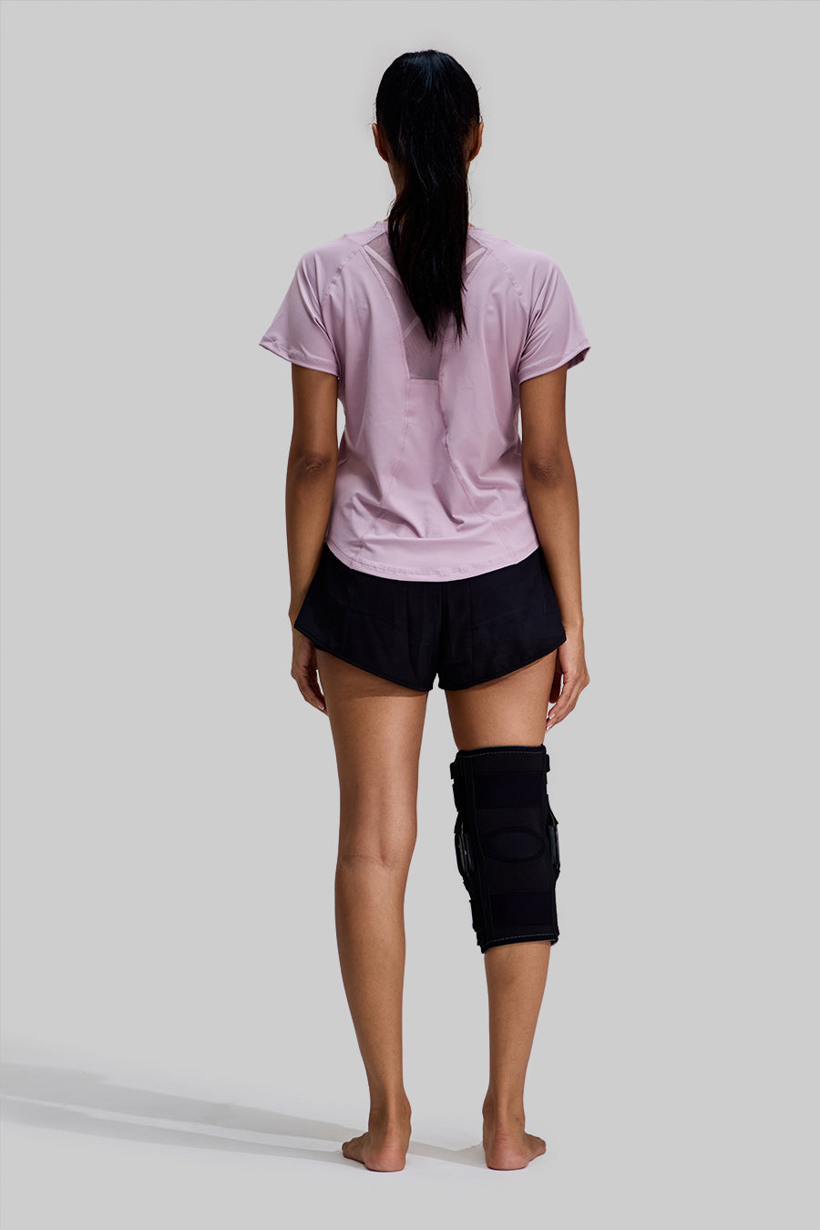Rear view of a female model wearing the NEENCA HX042/HX035 Hinged Knee Brace in Black, showing the full back coverage and ergonomic design