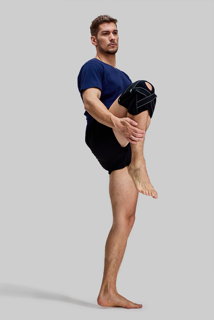 Side view of male model performing a standing knee-to-chest stretch wearing black NEENCA HX024 professional knee brace